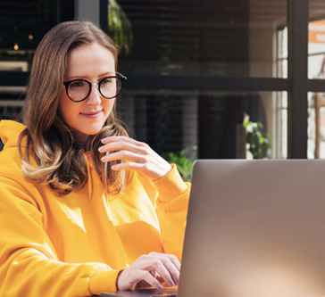 Image of woman in a yellow coat and her laptop, looking at social media